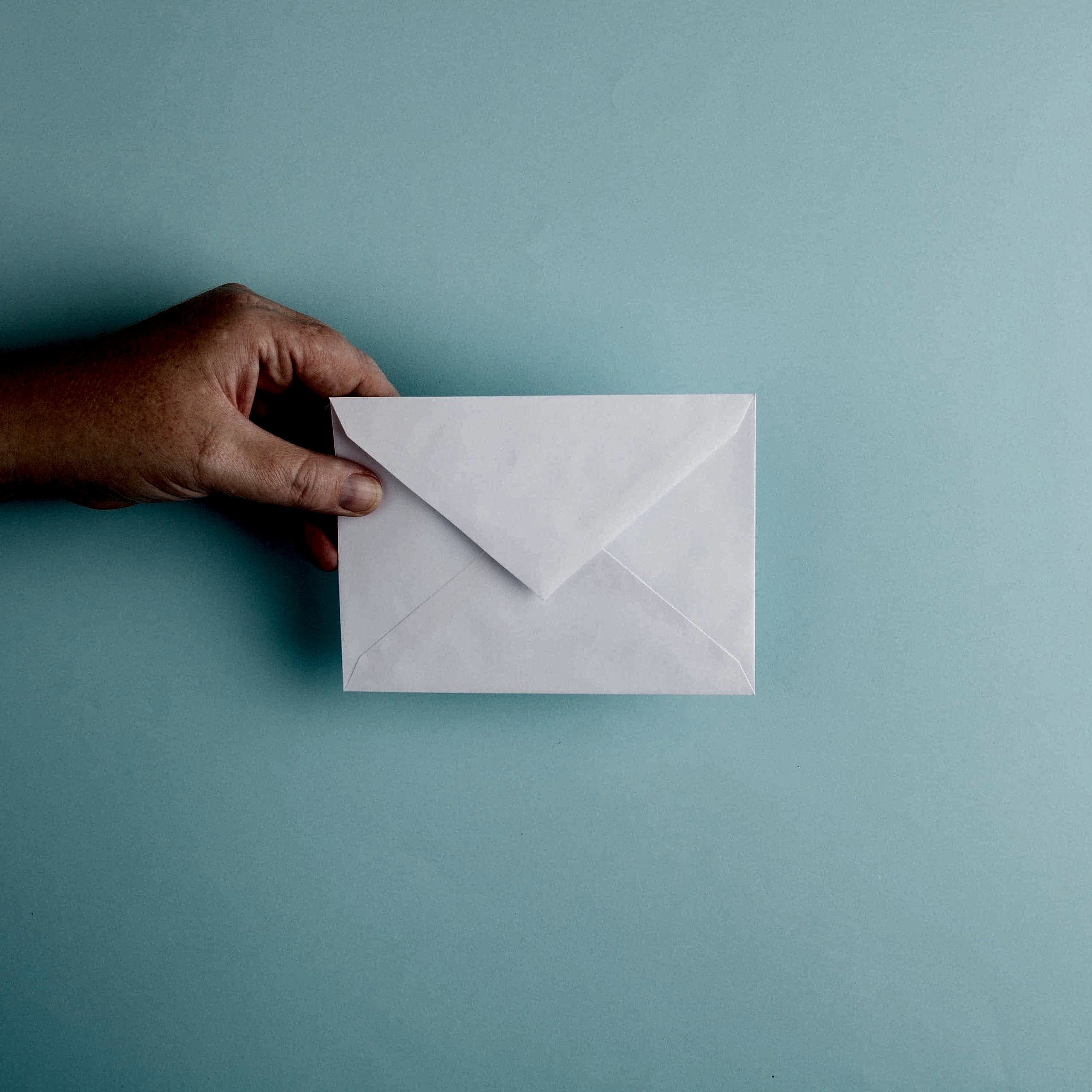 A hand holding a white custom invitation against a duck egg blue background